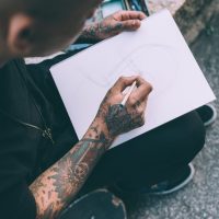 Close up on the hands of young hispanic man tattoed sketching on sketchbook - artist, drawning, creative concept