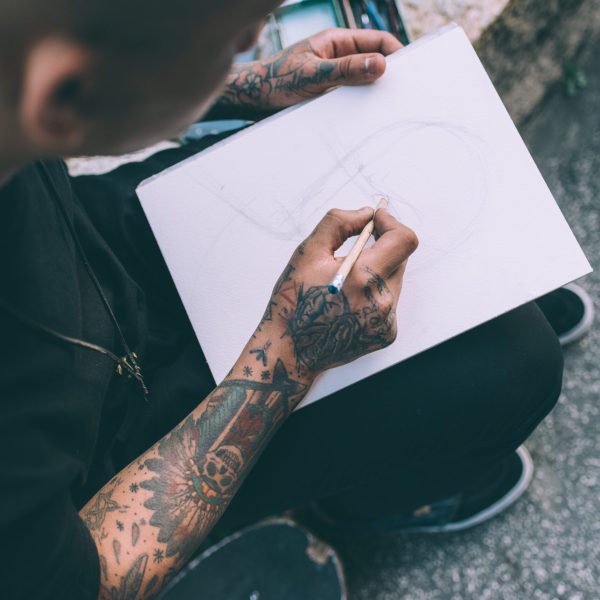 Close up on the hands of young hispanic man tattoed sketching on sketchbook - artist, drawning, creative concept