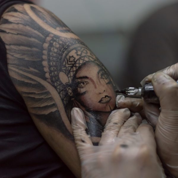 A closeup shot tattoo artist holding a tattoo machine tattooing a person