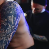 Tattooing. Man creating a picture on his back by a professional tattoo artist.
