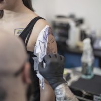 Tattooist removing tattoo stencil from woman's arm