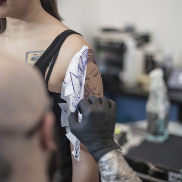 Tattooist removing tattoo stencil from woman's arm