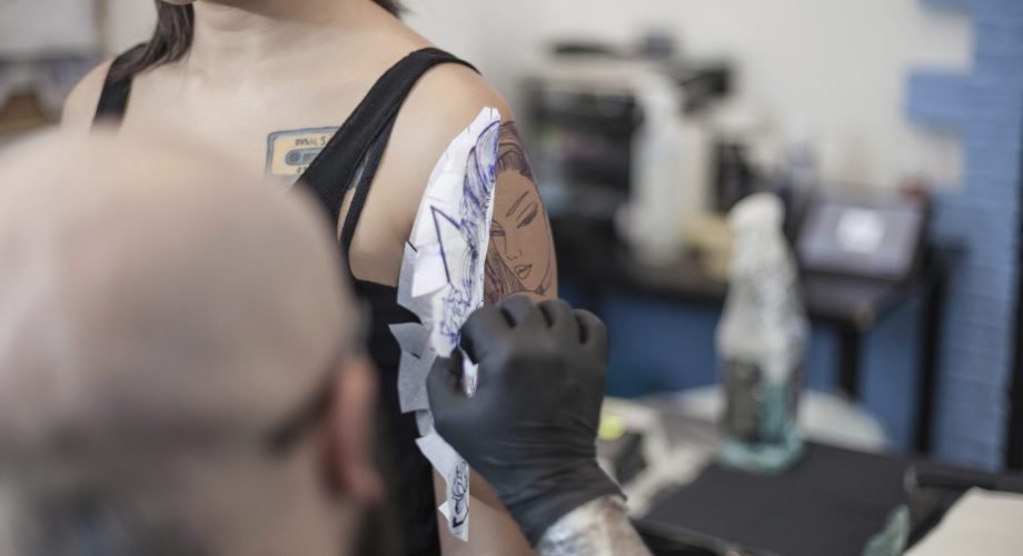 Tattooist removing tattoo stencil from woman's arm