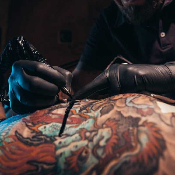 Cropped shot of an artist hands in a protective gloves holding ma machine while the ink is dropping