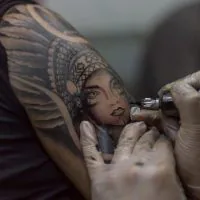 A closeup shot tattoo artist holding a tattoo machine tattooing a person