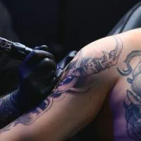 Tattoo artist hands wearing gloves and holding a tattoo machine.